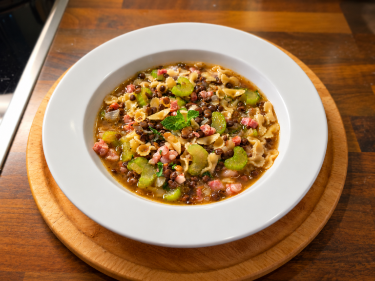 Sopa italiana de lentejas con farfalline, tocino, apio y menta fresca en plato blanco